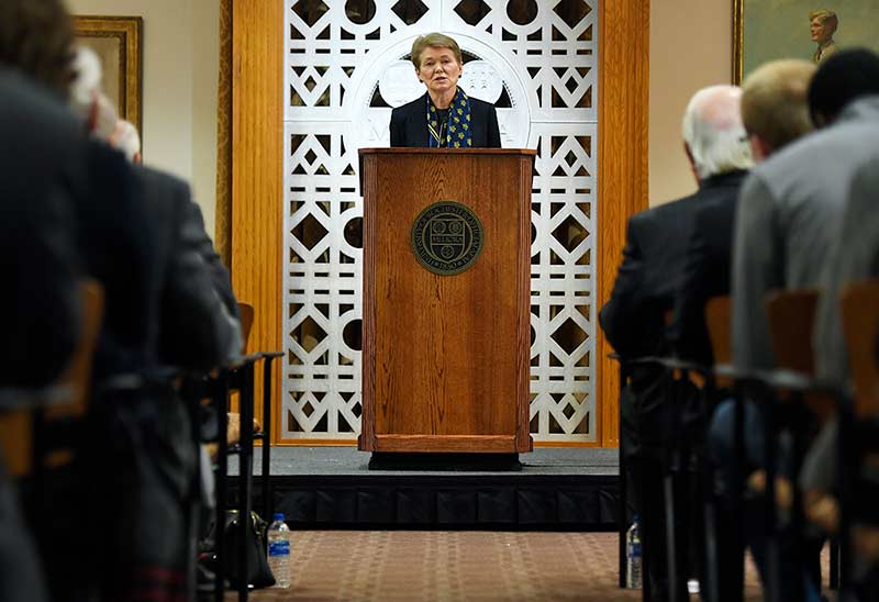 Sarah Mangesdorf standing at a podium with the MELIORA carving behind her