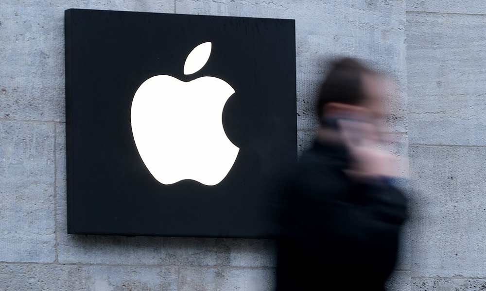 Feature image the Apple logo on a large sign on the side of a building, as a man walks past with an iphone to his ear