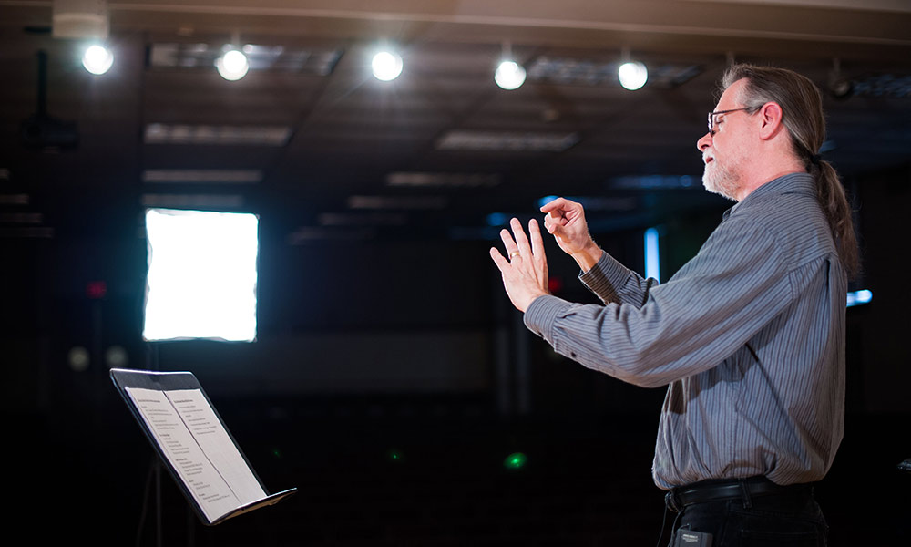 Feature image John Covach stands in front of a music stand, conducting