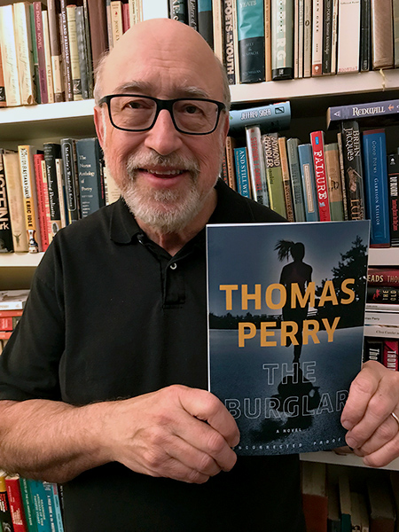 Thomas Perry poses in his office, holding a book with his name and the title THE BURGLAR on the cover