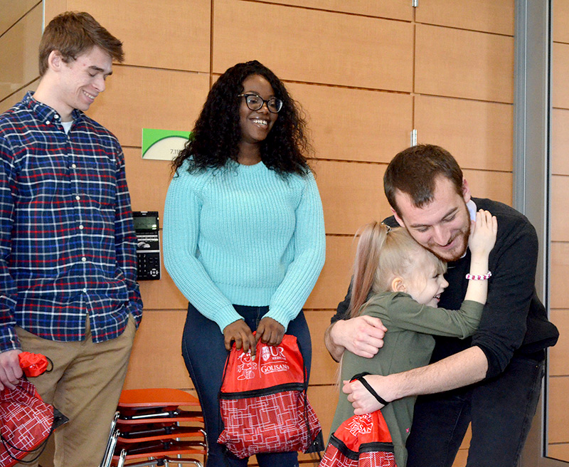 child hugs one college student as other student members of the team look on