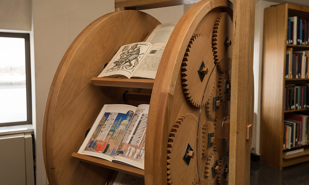 a large wooden wheel holds several book shelves and spins on a series of gears.