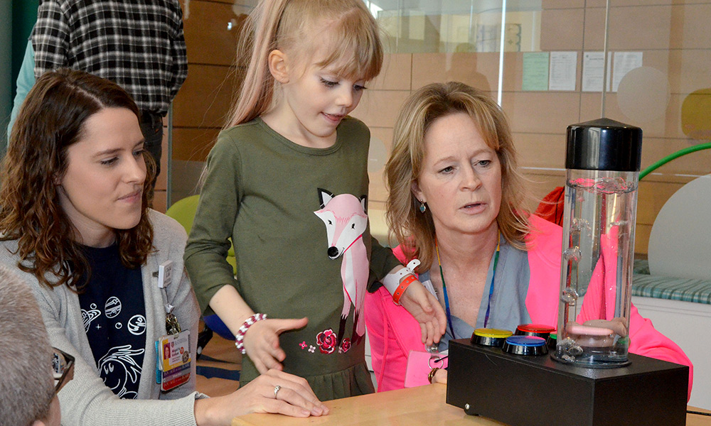 child in the middle, plays with a bubble toy with two adults