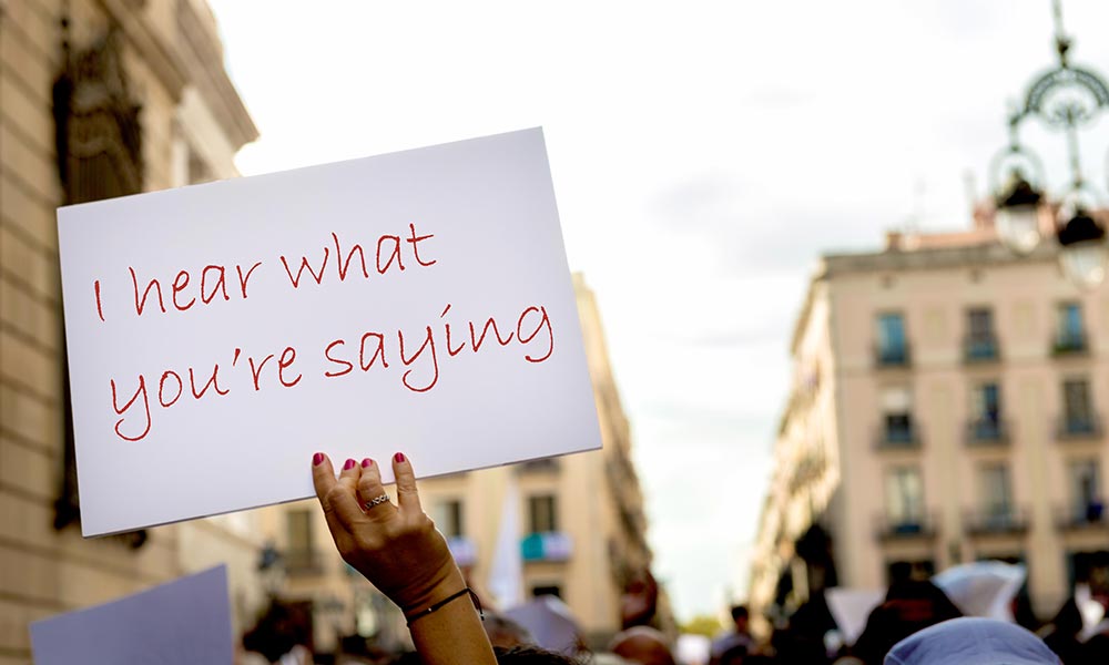 A protester holding a sign that reads I HEAR WHAT YOU'RE SAYING.