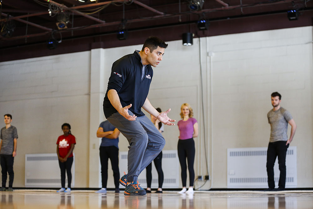 Feature image dancer makes exaggerated motions in front of a class in a dance studio.
