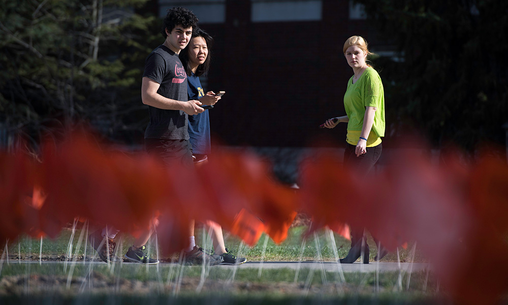 Feature image students walking past a large sea of small red flags planted in the ground in front of Wilson Commons.