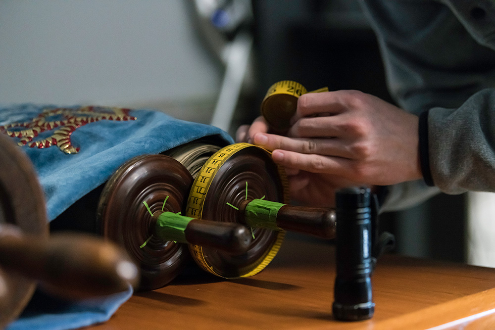 closeup of a torah scroll, with hands holding a tape measure around its edge