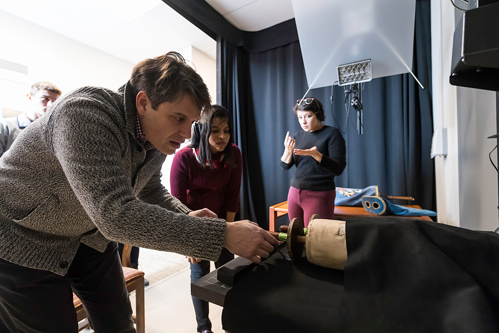 professor adjusts a scroll under the light of a scanner, as students watch.