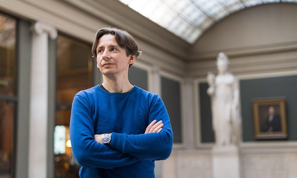 Jens Kipper poses for a portrait in front of the Romanesque statue of knowledge in Rush Rhees Library.