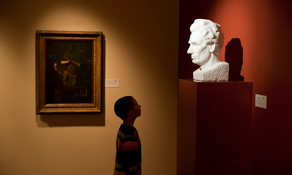child looks at marble bust of Abraham Lincoln in a museum.