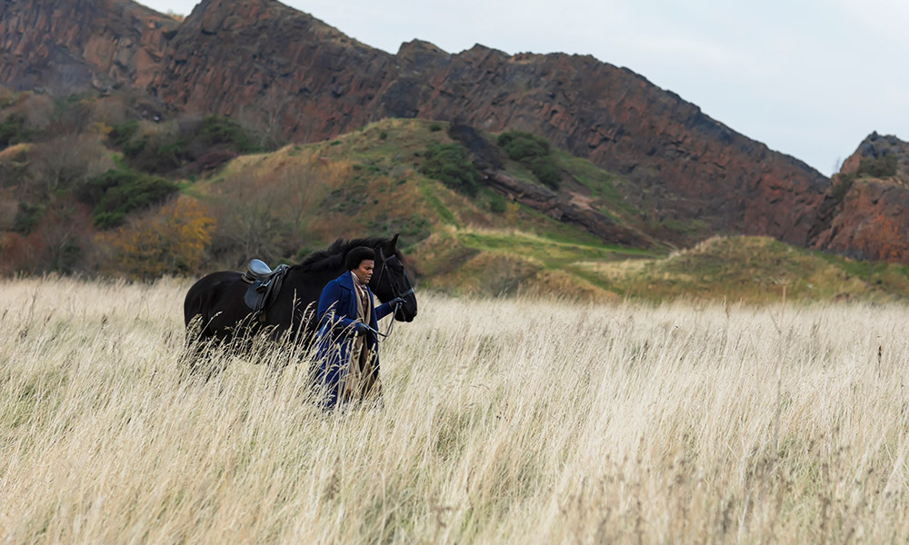 Feature image video still of an actor playing Frederick Douglass, walking a horse through a field