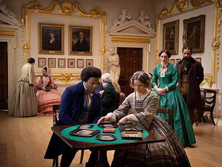 still from a video screen of Lessons of the Hour installation shows actors portraying Frederick Douglass and other guests in a British drawing room