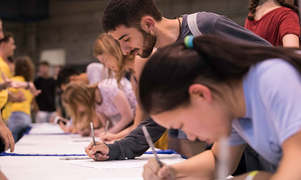 large line of student signing a roll of parchment.
