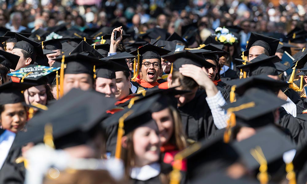 crowd of graduates with one student in sharp focus, smiling and waving