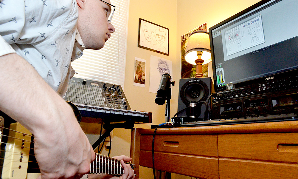 student plays a guitar while looking at a computer screen