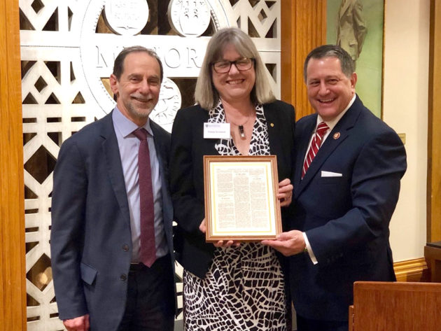 three people pose for a photo, holding a framed document