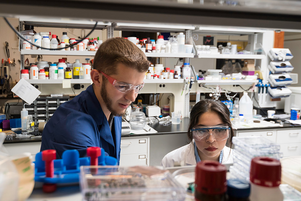 two researchers in safety goggles in the lab looking at samples