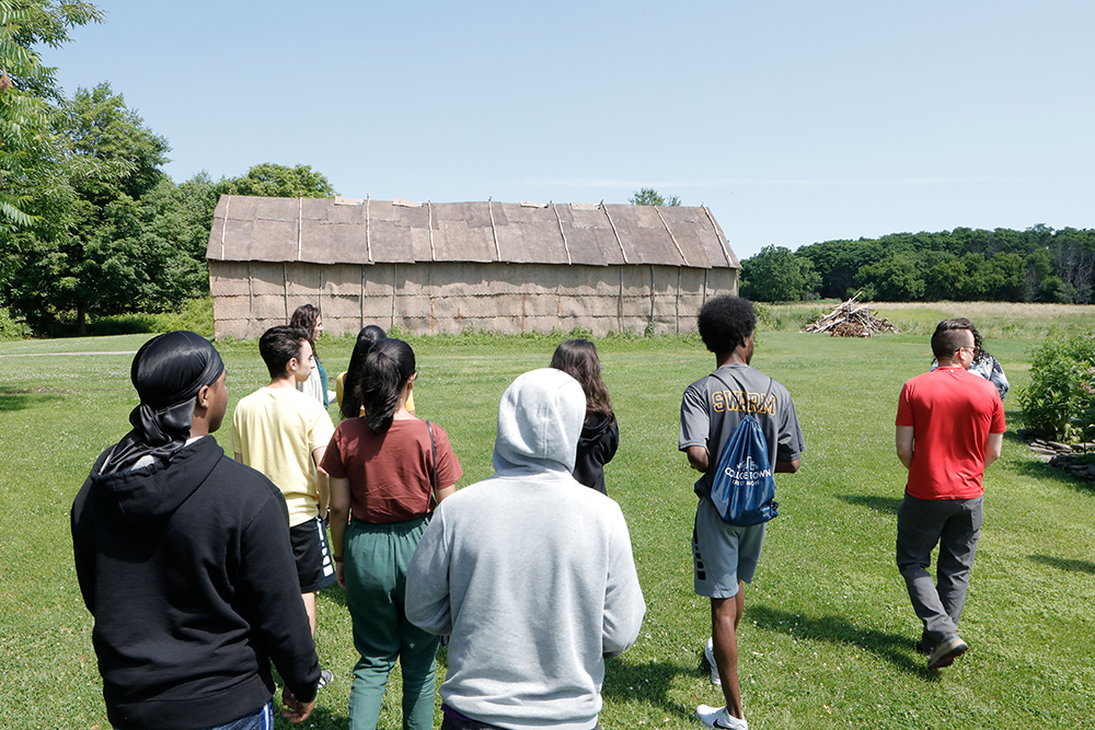 group of students waking toward a Native American longhouse