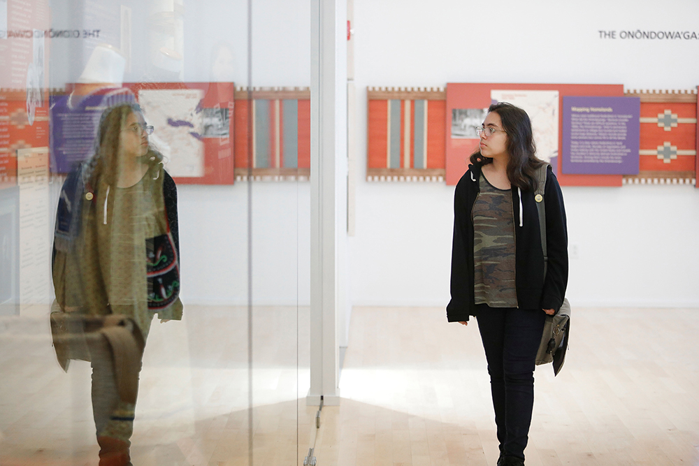 student walking through an art exhibit is reflected in the exhibit's glass walls.