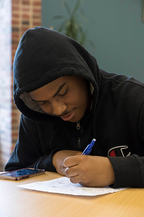 student at a desk, writing on a piece of paper. 