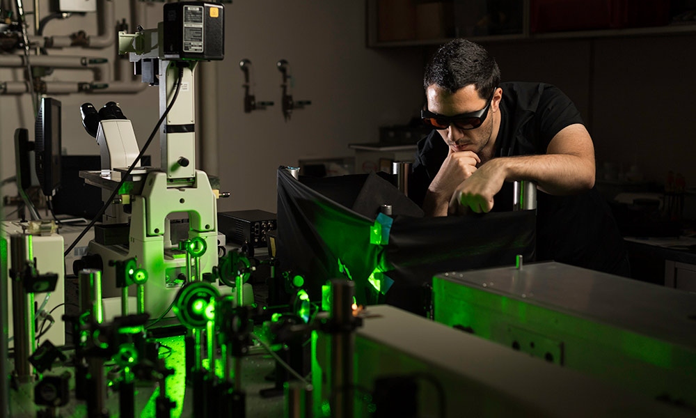 student researcher in safety glasses working in an optics lab.