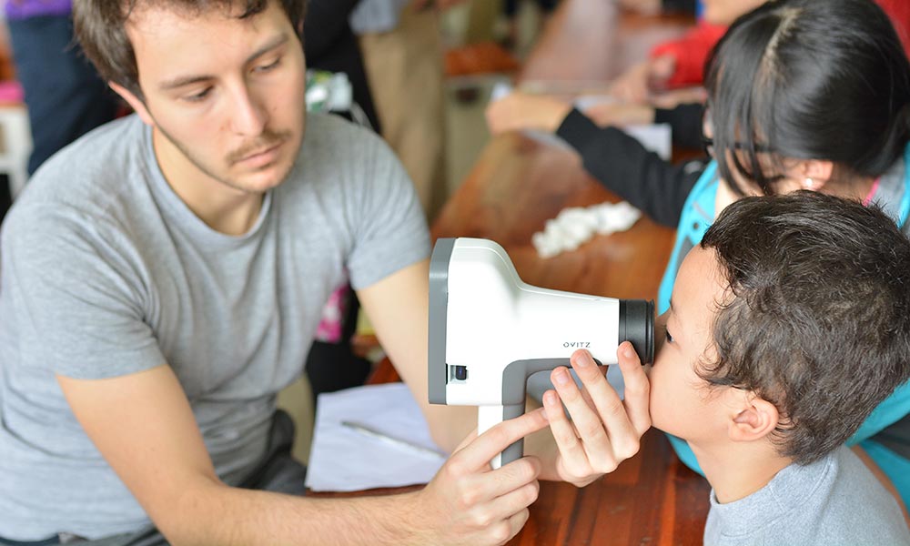 technician holds a device in front of the eyes of a young child, who looks through the device