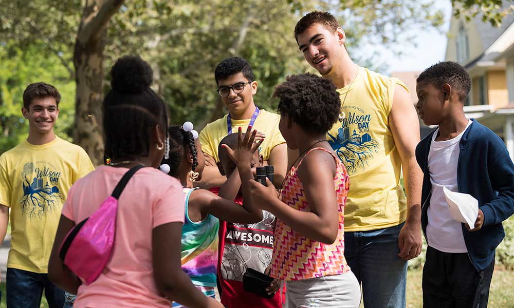 group of college students in matching t-shirts giving kids high-fives