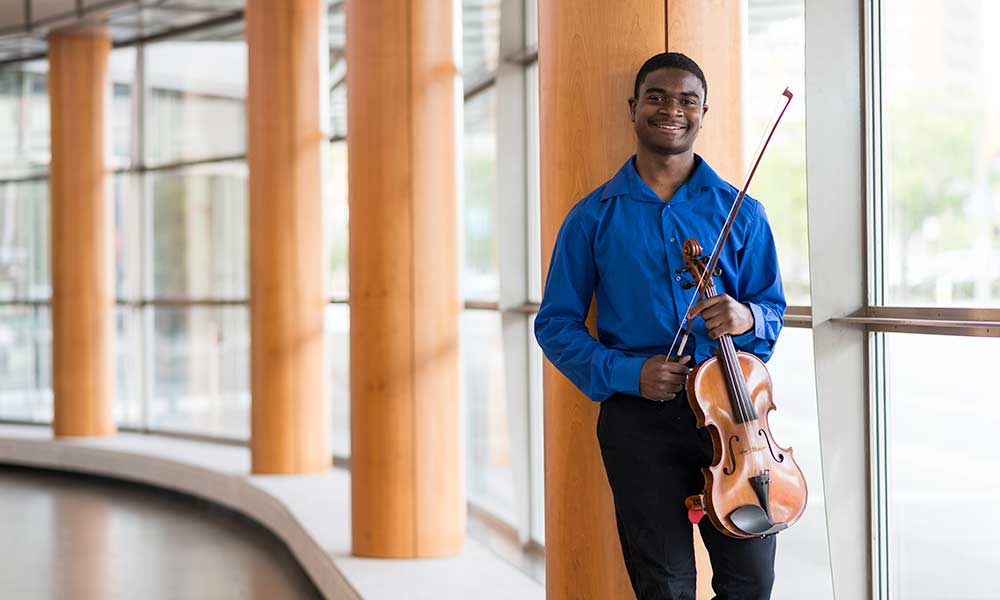 Student stands posing with viola in well-lit hallway.