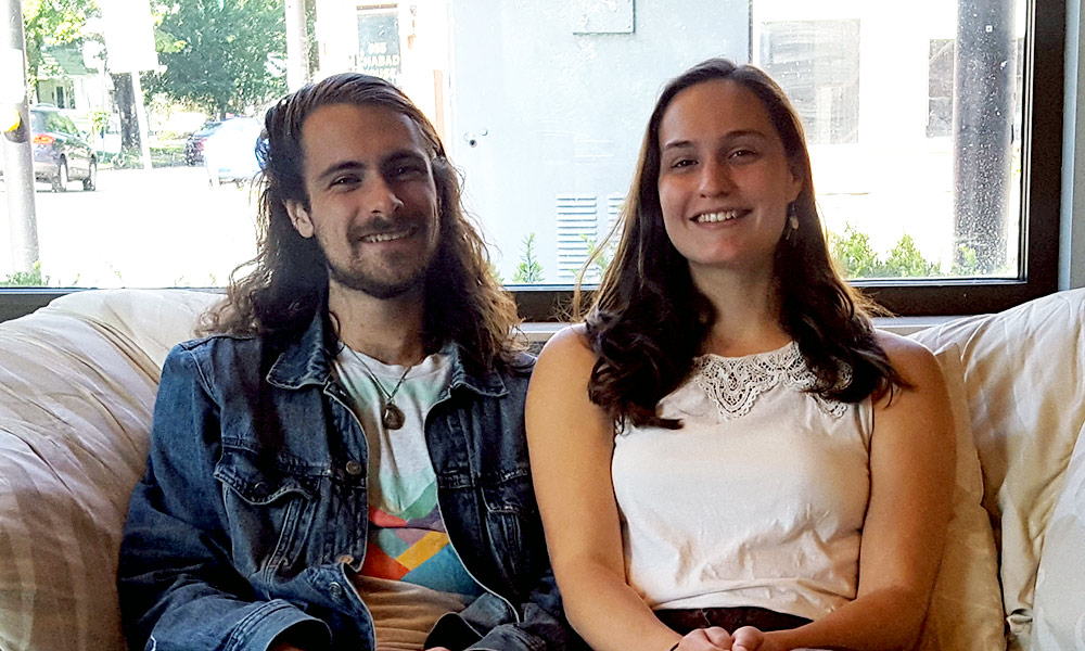 two people pose for a photo, smiling, sitting on a coach.