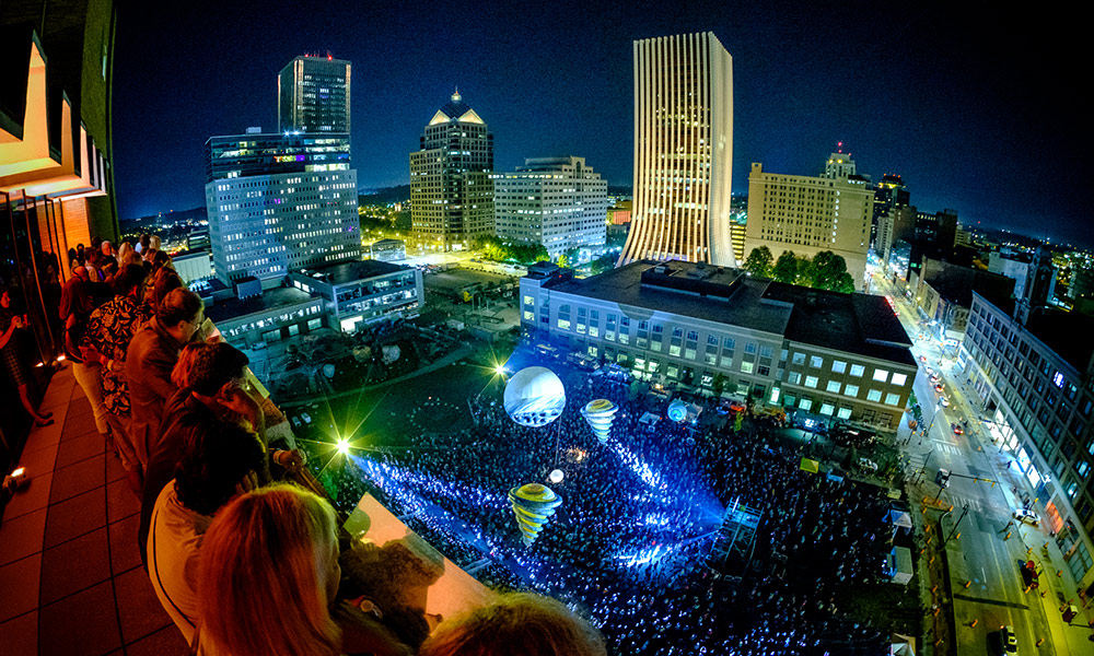 Overhead view of a high crowd in downtown Rochester watching a display of giant balloons.