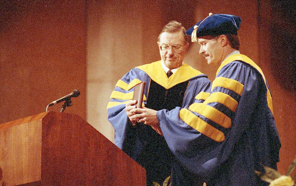 two men in academic robes, one presenting the seal to the other. 
