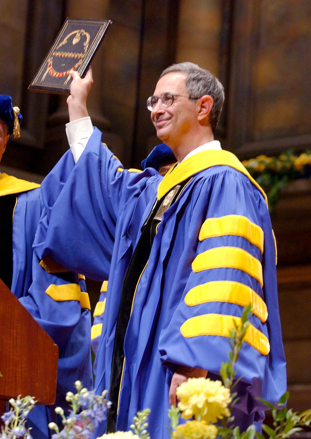 President Seligman in academic robes holds up University charter.