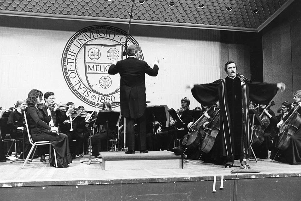 Singer wearing acaedmic robes performs on stage