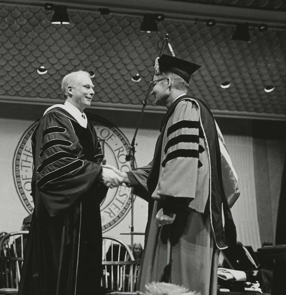 Four men on stage in academic robes, shaking hands
