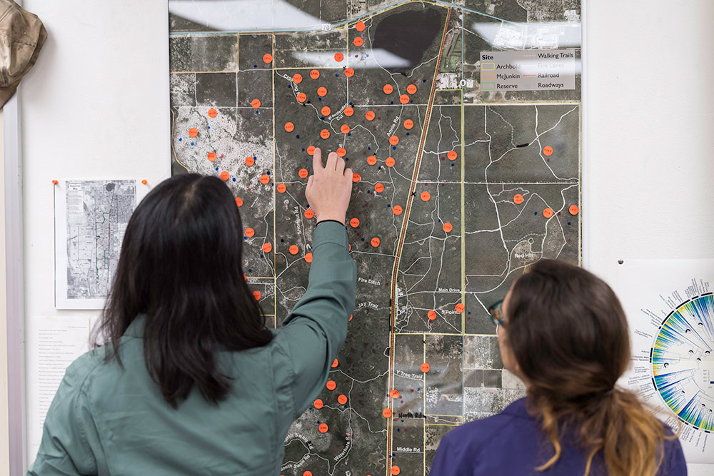 two researchers look at orange dots plotted on a wall map