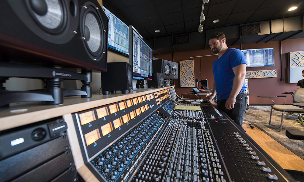 professor Steve Roessner stands in front of a large sound board in a recording studio.