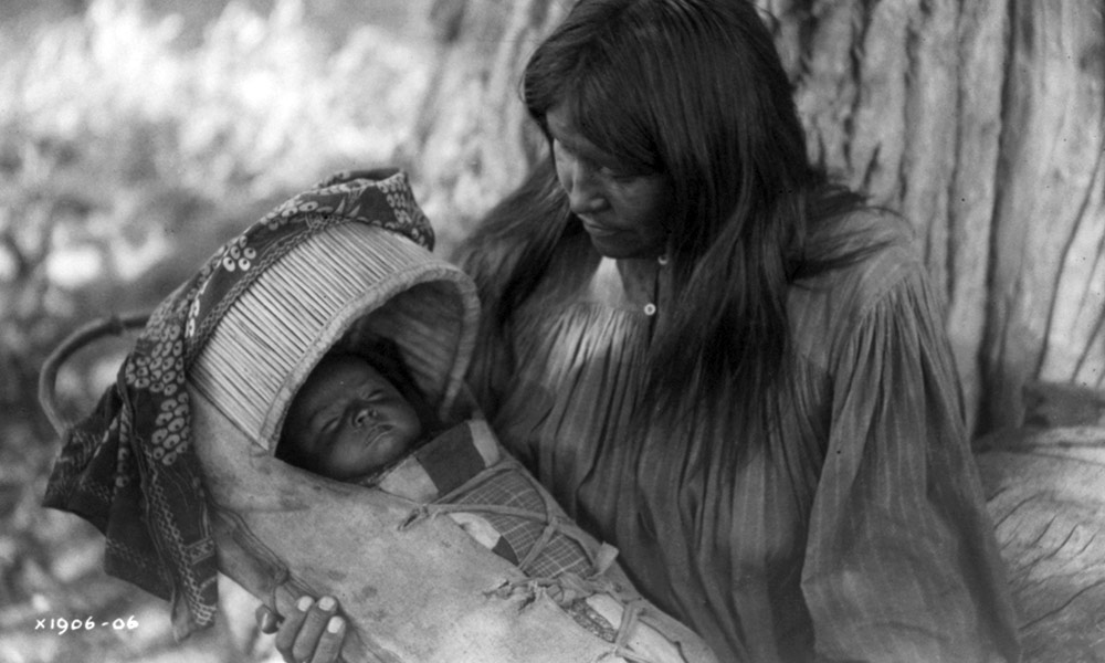 historical image of a Native American mother holding a child in a papoose