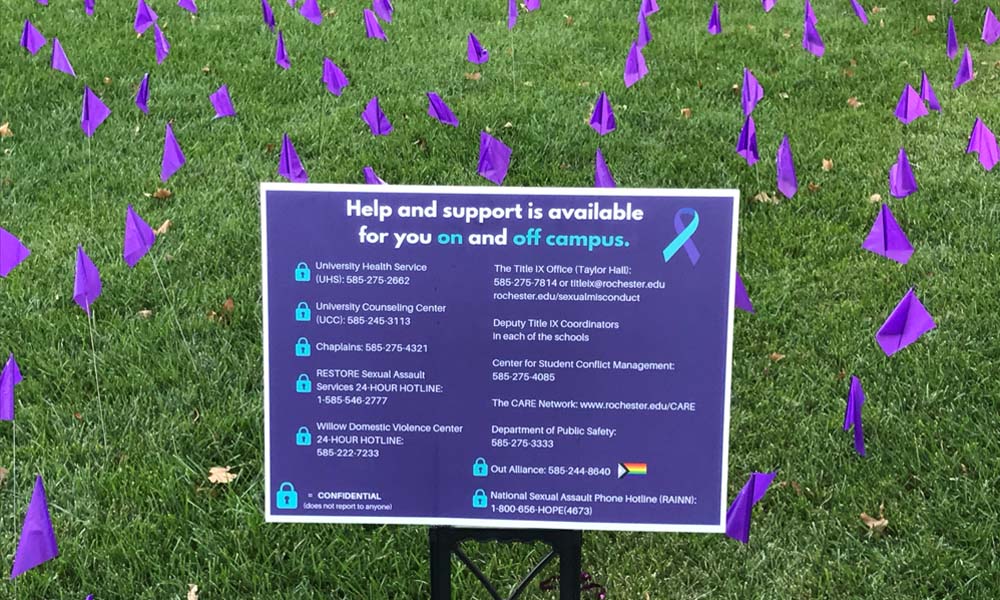 Purple sign on the Hajim Quad with purple flags behind it.