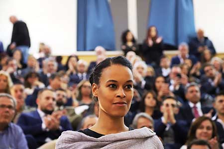 professor stands before an audience of people applauding.