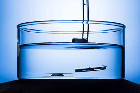 two metallic structures submerged in water, one floating to the surface after a weight placed on top if it has been removed.