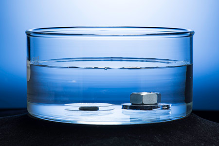 two metal discs submerged in water, one superhydrophobic disc weighted down by a metal washer and nut