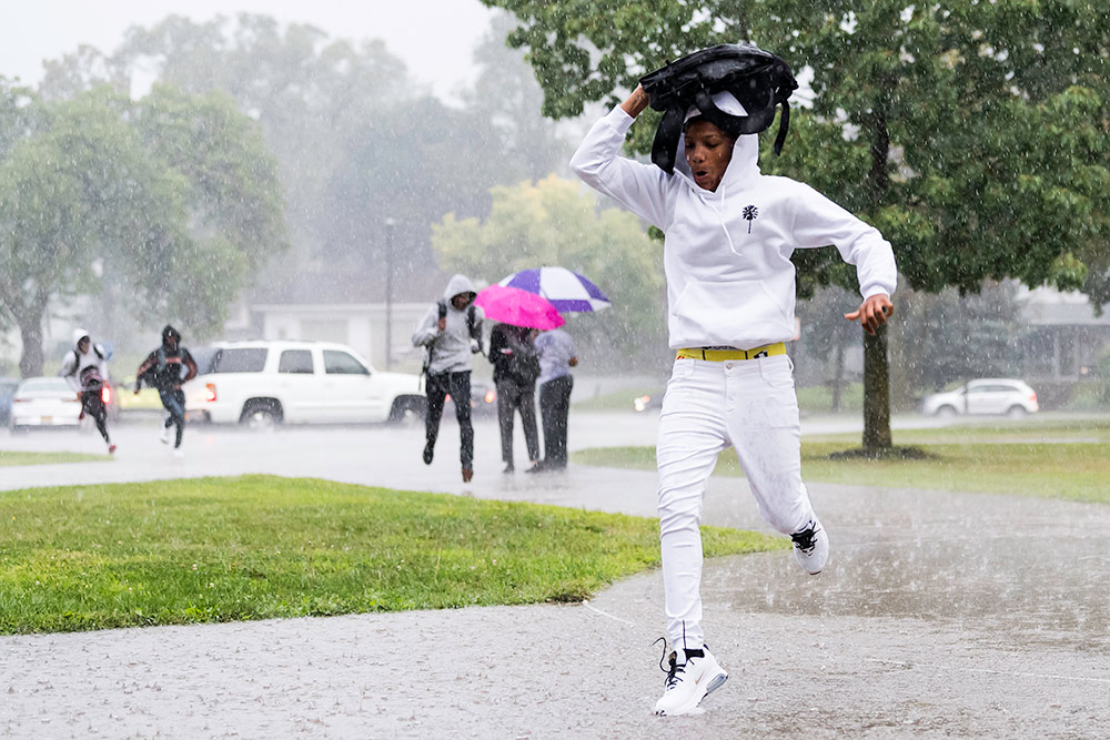 student running through the rain with his backpack over his head.