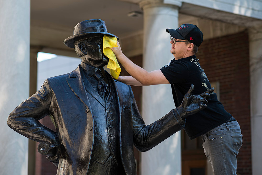 person on a ladder uses a cloth to clean the face of a statue.