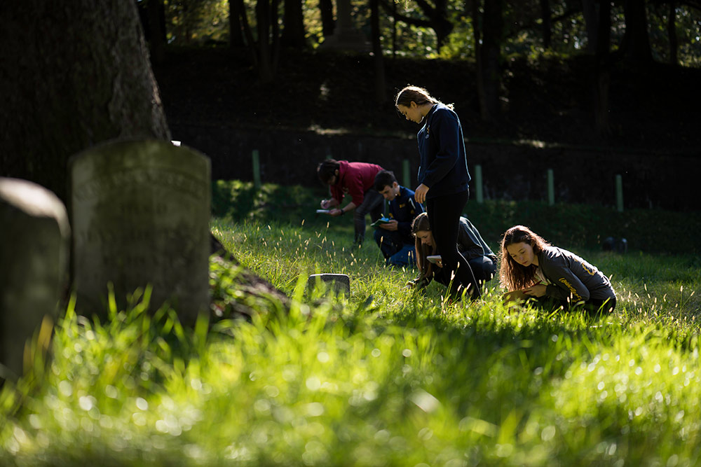 students crouching in the grass in Mount Hope Cemetery.