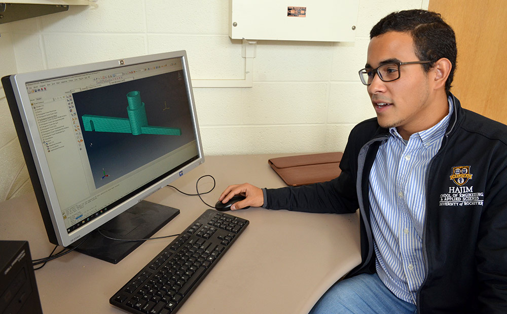 student sits in front of a computer screen with a 3d model on it.
