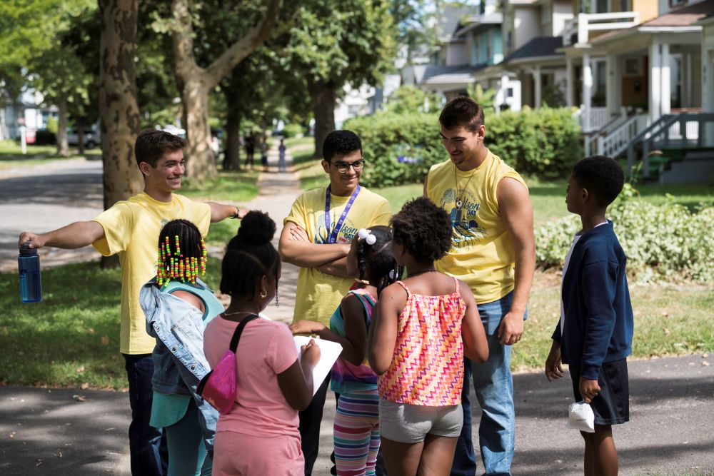 group of students speaking with children, all standing in a circle