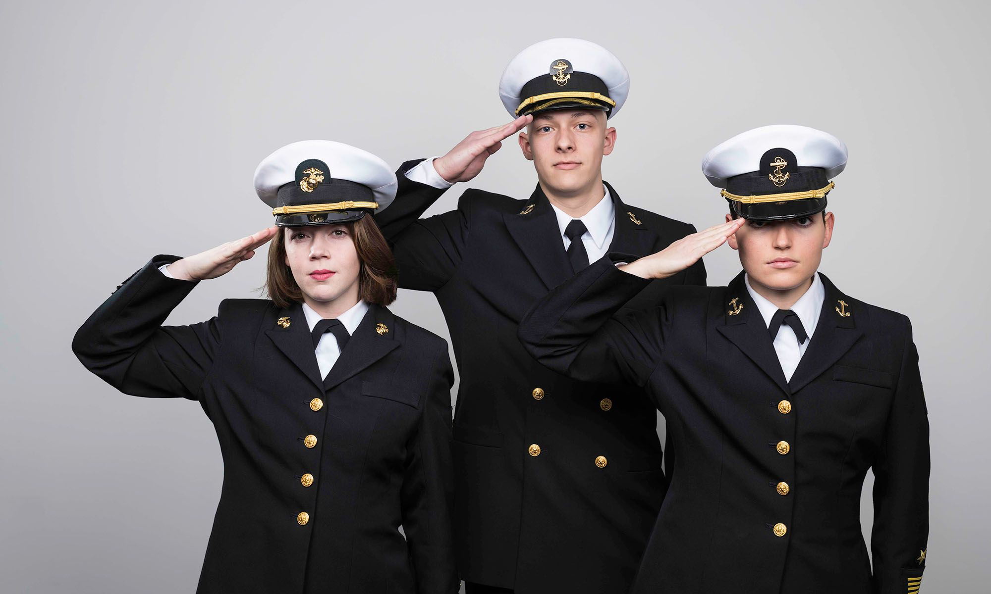 Three University of Rochester NROTC midshipmen in uniform saluting the camera.