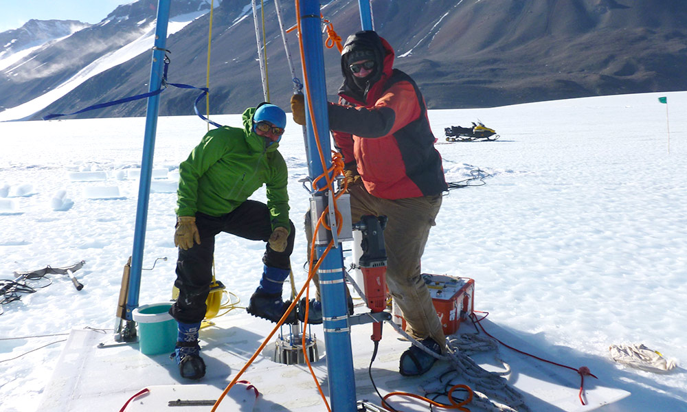 two scientists pose at ice drill in Antarctica.