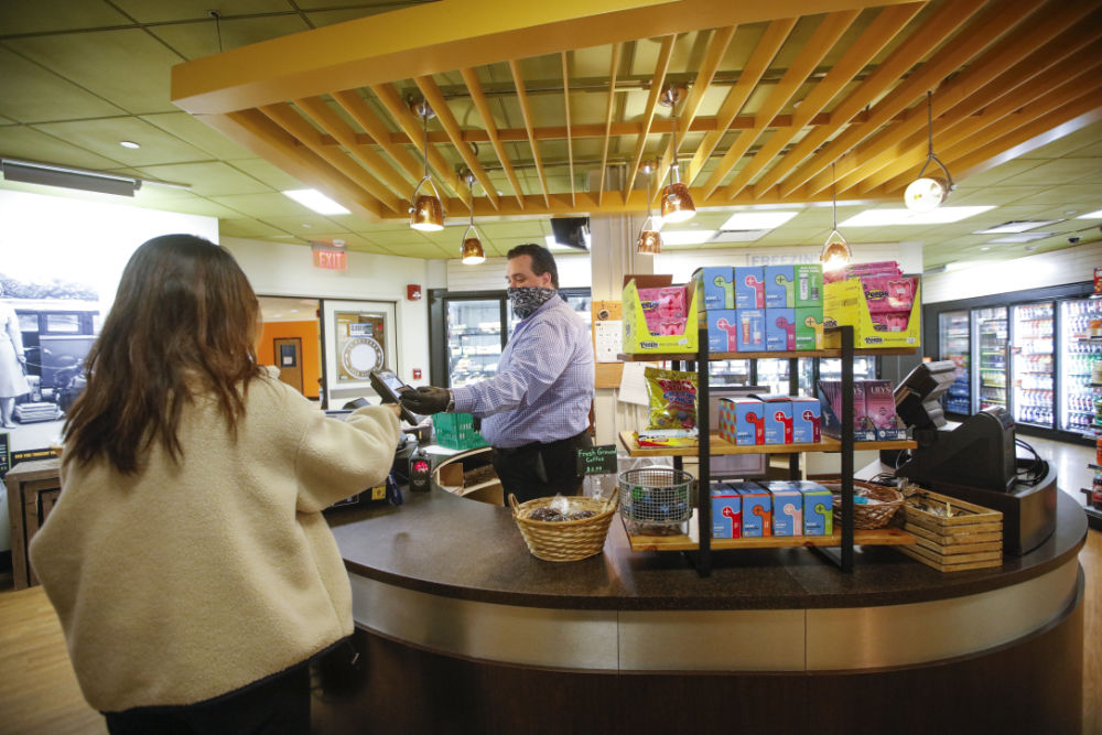 Brant Lewis, donning a face mask, cashes out a student, seen from behind, at Hillside Market.