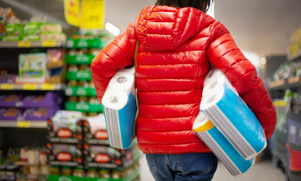 Woman at supermarket carries three large packages of toilet paper